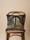 A square woven tapestry pillow with two howling wolves on a black background. The wolves are surrounded by pink and green botanical flowers, creating a vintage, folkloric scene. This decorative cushion is perfect for cottagecore, dark academia, and gothic home decor.